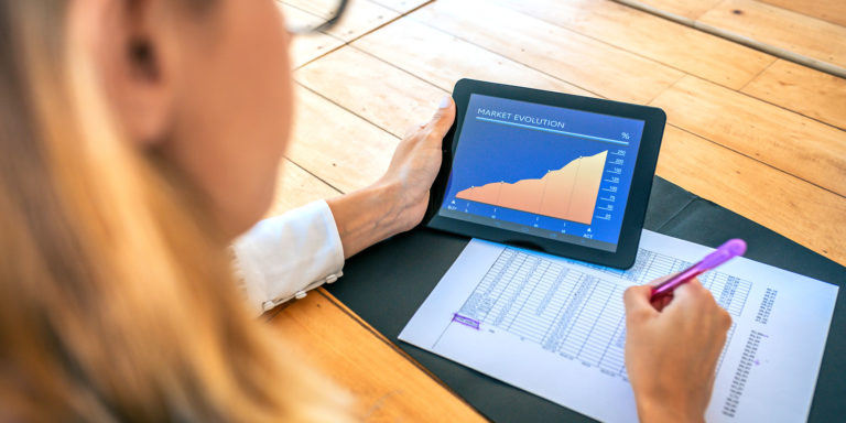 A business professional analyzing market trends on her tablet and taking notes with a pen, Caber Hill Advisors