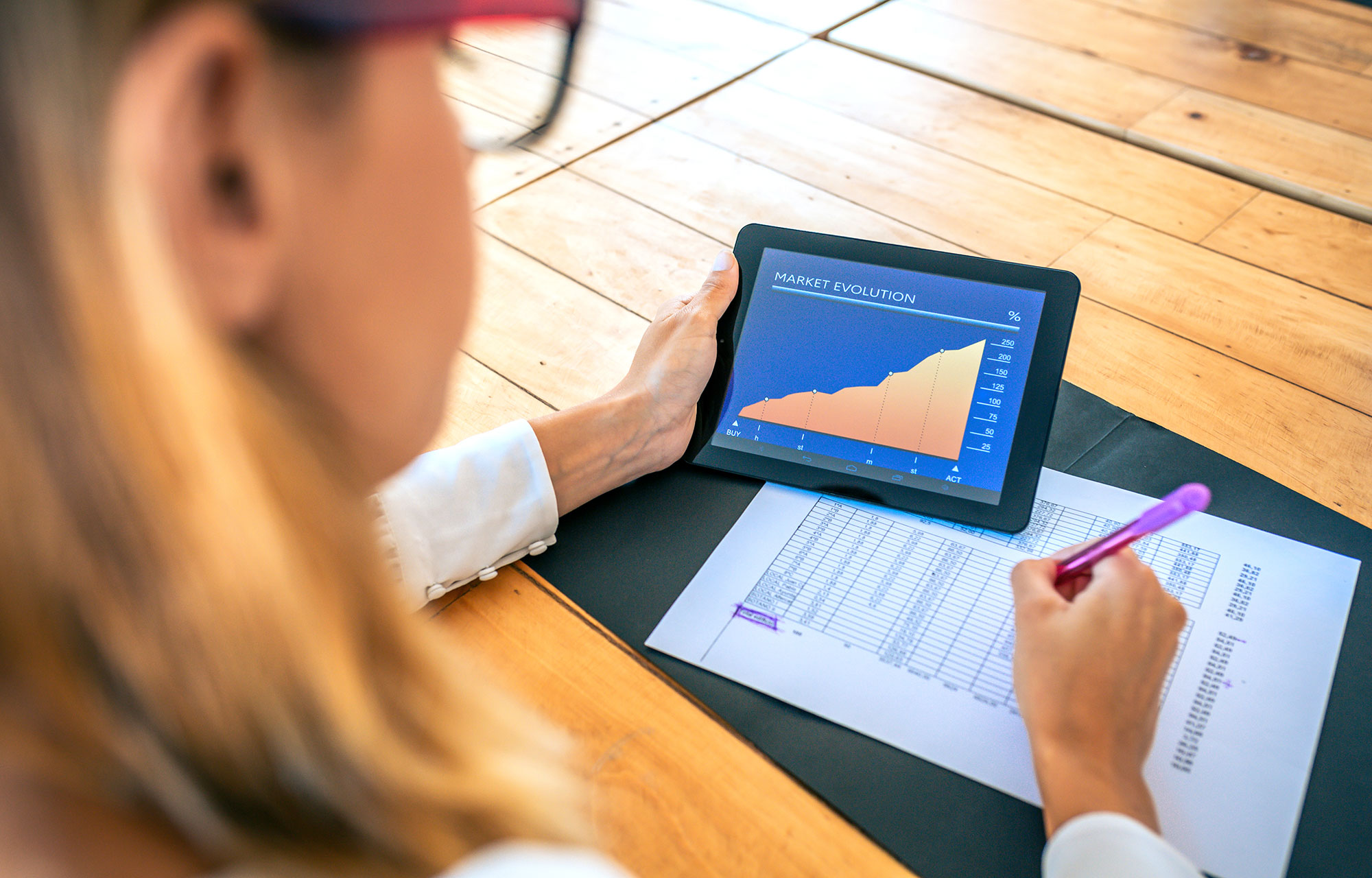 Analyzing-Market-Trends A business professional analyzing market trends on her tablet and taking notes with a pen, Caber Hill Advisors