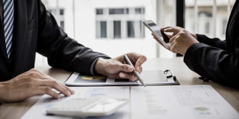 Two business professionals in a conference room reviewing analytics while using a calculator and a phone, Caber Hill Advisors