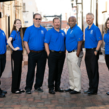A group of seven business professionals in blue polos and black pants lined up to take a photo, Caber Hill